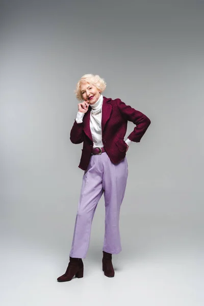 Улыбающаяся Пожилая Женщина Стильной Одежде Смотрящая Камеру Сером — Бесплатное стоковое фото
