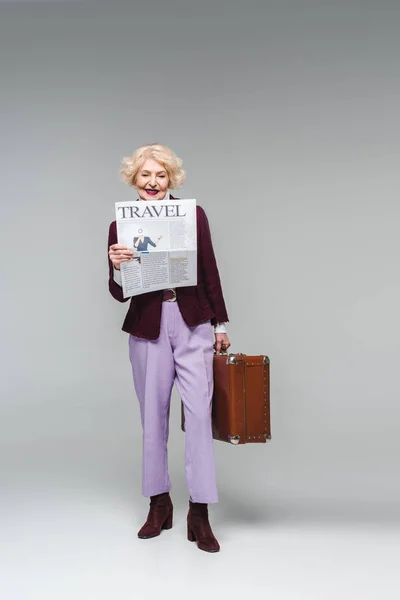 美しいシニア女性スーツケースを押しながらグレーの旅行新聞を読む — ストック写真