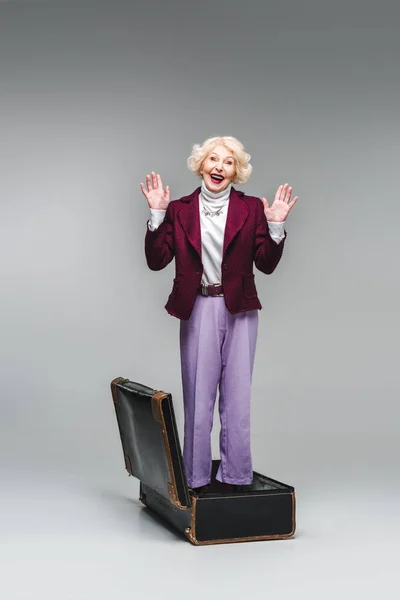 Happy Senior Woman Standing Vintage Suitcase Raised Hands Grey — Stock Photo, Image