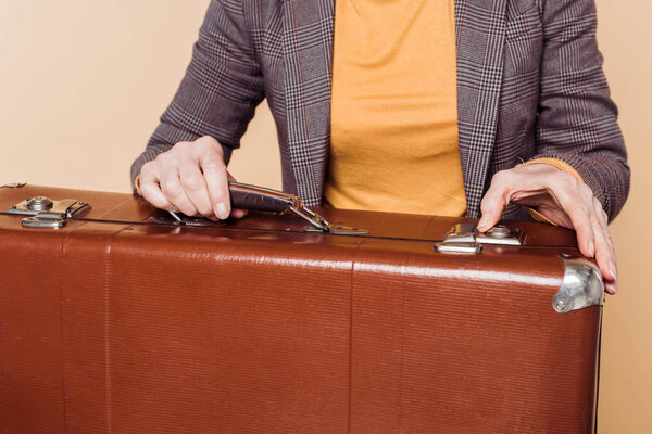 cropped shot of stylish woman closing vintage suitcase isolated on beige background 