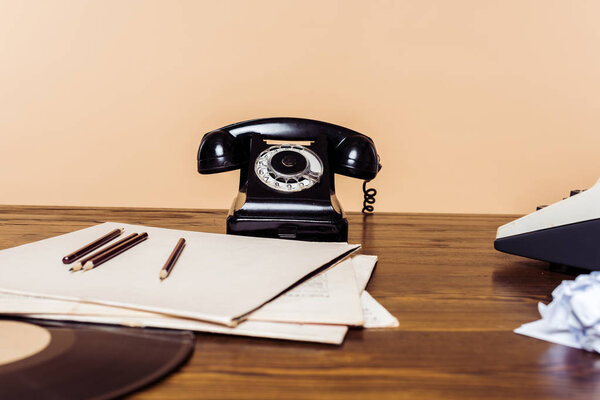 closeup shot of rotary phone on wooden table with typewriter and vinyl disc on table 