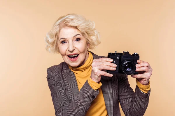 Überraschte Seniorin Mit Filmkamera Auf Beigem Hintergrund — Stockfoto