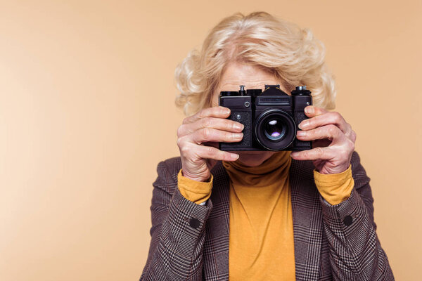 senior woman shooting on film camera isolated on beige background 