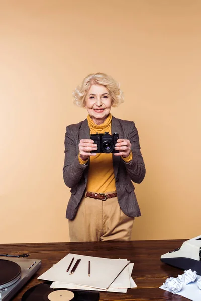 Улыбающаяся Стильная Пожилая Женщина Пленочной Камерой Бежевом Фоне — Бесплатное стоковое фото
