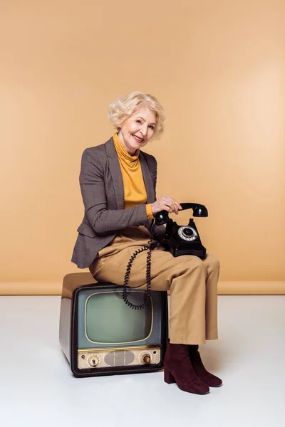 Lächelnd Stilvolle Seniorin Mit Drehhandy Sitzt Auf Vintage Fernseher — Stockfoto