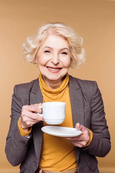 ベージュ色の背景に分離されたコーヒー カップと幸せのファッショナブルな年配の女性 — ストック写真