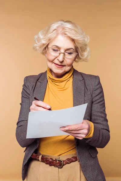 Stylische Seniorin Mit Brille Die Auf Papier Auf Beigem Hintergrund — kostenloses Stockfoto