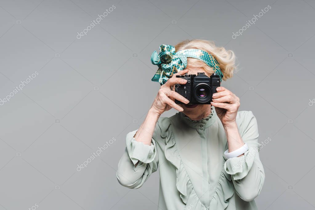 Stylish senior woman taking photo with vintage film camera isolated on grey stock vector