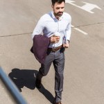 Vista de ángulo alto de joven hombre de negocios guapo con taza de papel de café corriendo para el trabajo