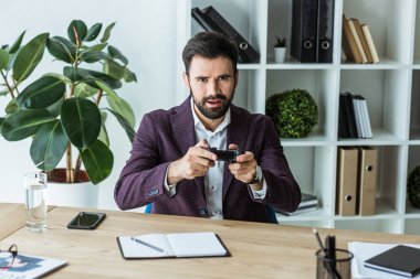 İşyerinde otururken kameraya bakarak gamepad ile yakışıklı genç işadamı
