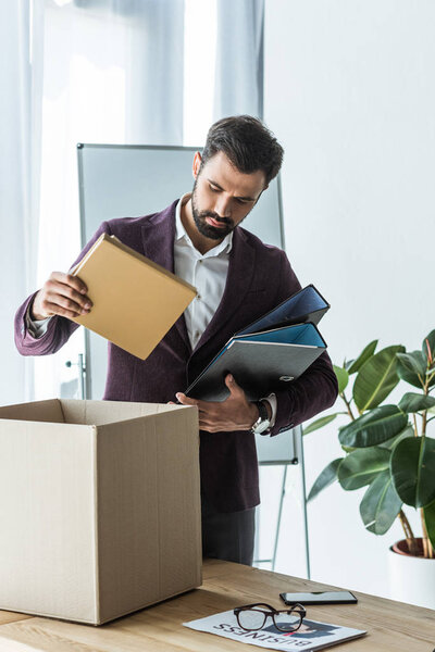 dismissed young businessman putting books and folders into box