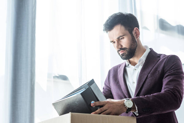 thoughtful young businessman putting books and folders into box after he gets fired