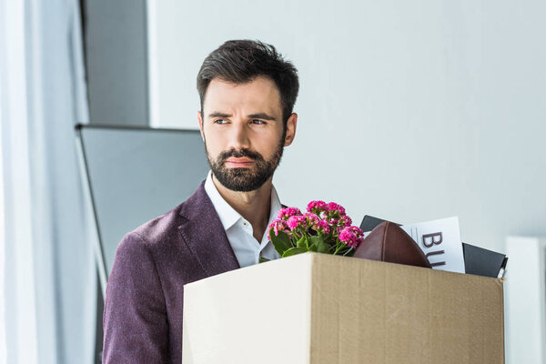 depressed young businessman carrying box of personal stuff after he gets fired
