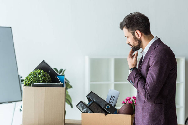 side view of thoughtful young businessman looking at boxes of personal stuff after he gets fired
