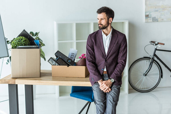 thoughtful young businessman with boxes of personal stuff leaning back on desk at office