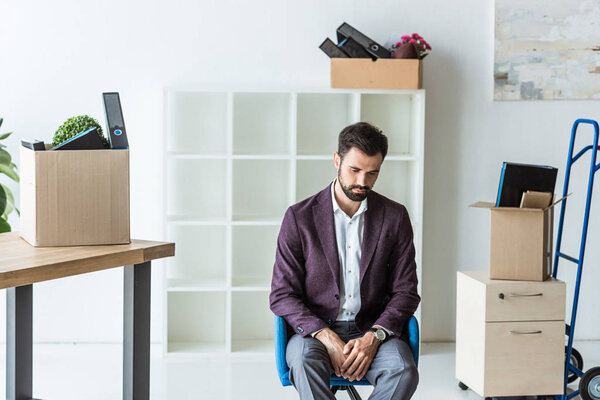 depressed fired businessman sitting on chair in office with boxes of personal stuff