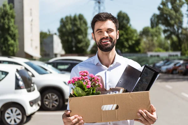 happy young manager with box of personal stuff on parking