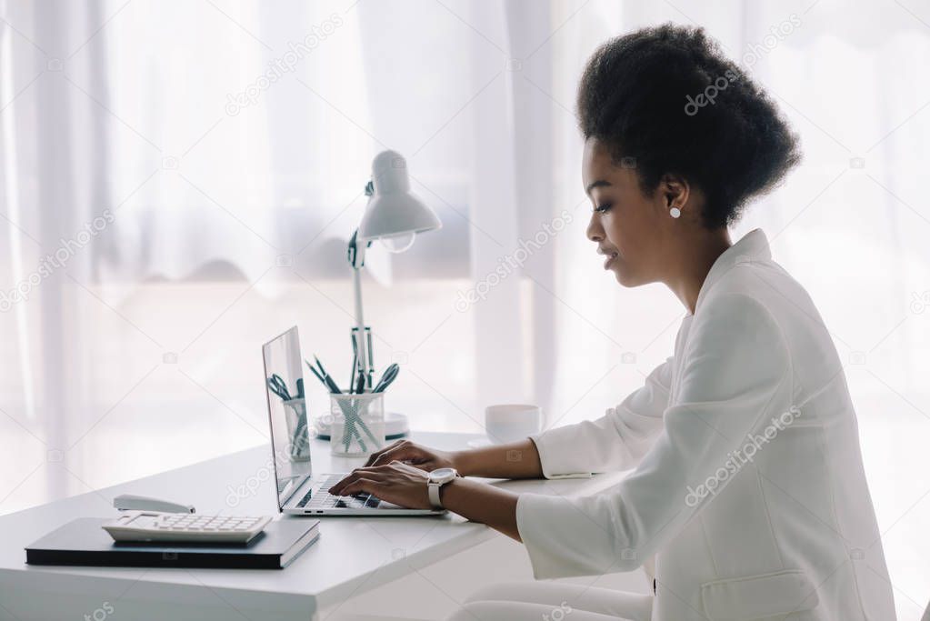 side view of attractive african american businesswoman using laptop in office