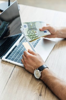İşyeri dizüstü bilgisayar ile kredi kartı ve euro banknot tutan kişinin kısmi görünümü