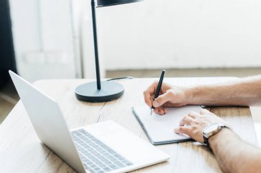 Not alma ve laptop ile masada çalışan kişi resmini kırpılmış