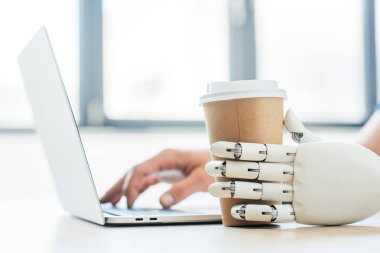 Robotik Kol tutan tek kullanımlık kahve fincanı ve insan eli dizüstü kullanarak yakından görmek  