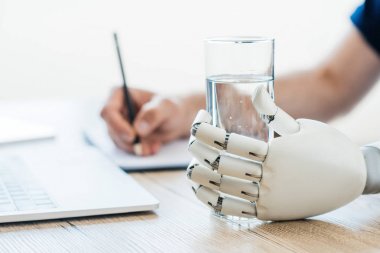 seçici odak robot kolunun su ve kişi not almak ahşap masa tutarak. 