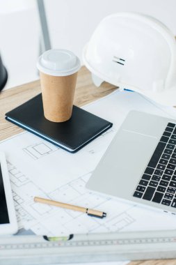 dizüstü bilgisayar, plan, defter, tek kullanımlık kahve fincanı ve işyerinde zor şapka