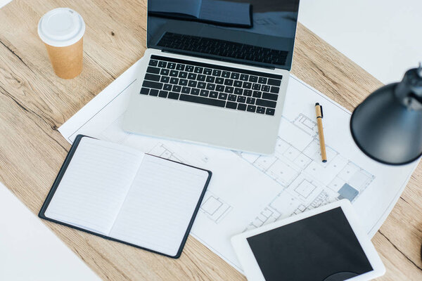 high angle view of laptop, digital tablet, notebook and blueprint on wooden table