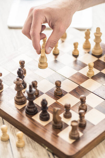 close-up partial view of person playing chess at wooden table