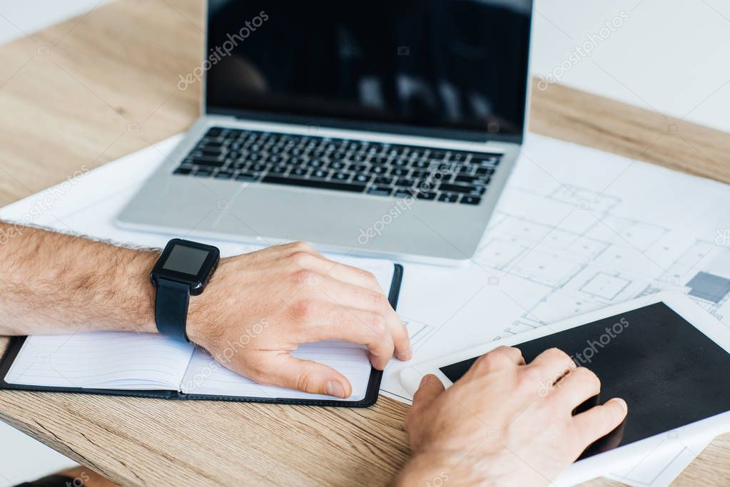 cropped shot of person wearing smartwatch and using digital tablet at workplace