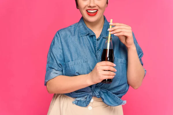 cropped shot of smiling pin up woman holding glass bottle with drinking straw isolated on pink