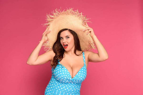 beautiful surprised size plus woman in straw hat looking at camera isolated on pink
