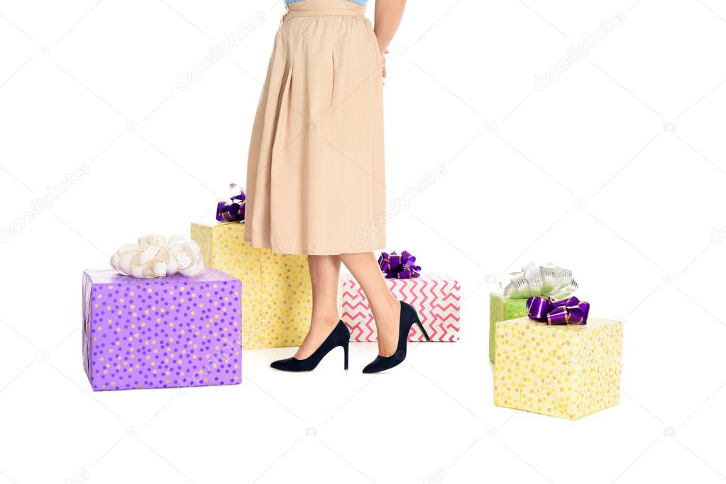 low section of stylish woman in skirt and high heeled shoes standing near gift boxes isolated on white
