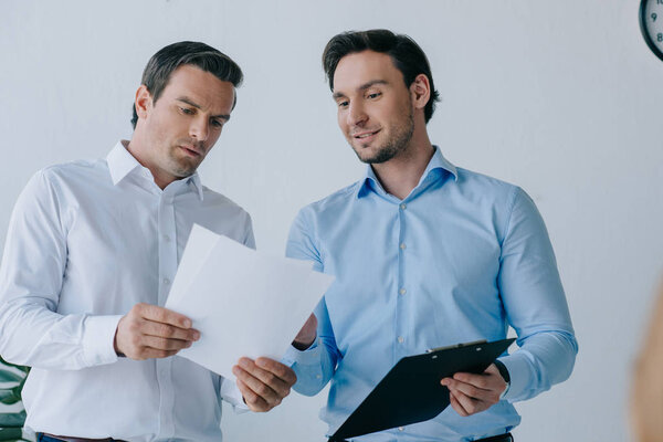 portrait of businessmen with papers discussing work in office