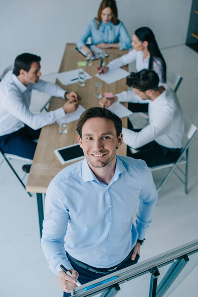 selective focus of smiling businessman at white board and coworkers at workplace in office
