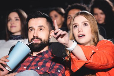 Kağıt bardaklı yakışıklı erkek arkadaş ve çekici kız arkadaş parmaklarıyla işaret edip sinemada film izliyor. 