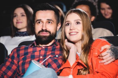 Yakışıklı erkek arkadaş gülümseyen kız arkadaşa sarılıyor ve sinemada film izliyor. 