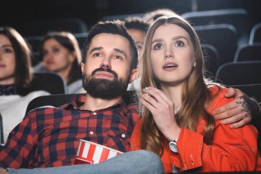 Yakışıklı erkek arkadaş şok olmuş kız arkadaşına sarılıyor ve sinemada film izliyor. 