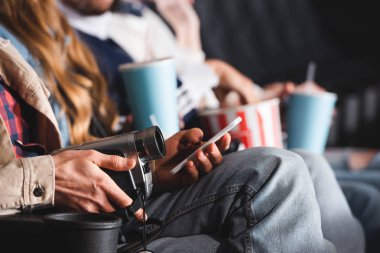 Dijital kamerayla çekim yapan ve sinemada akıllı telefon kullanan adam görüntüsü.
