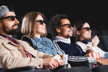 Üç boyutlu gözlüklü çok kültürlü arkadaşlar sinemada gülümsüyor ve film izliyorlar. 