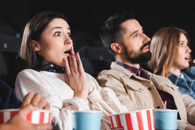 Sinemada arkadaşlarıyla film izleyen şok olmuş bir kadının seçici odağı 