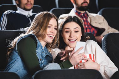 Sinemada akıllı telefona bakarak gülümseyen arkadaşlara odaklan 