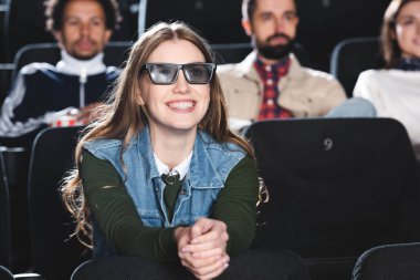 Üç boyutlu gözlüklü gülümseyen kadının sinemada film izlediği seçici odak noktası. 