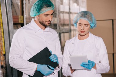 Yakışıklı bir dükkan sahibi dijital tablet kullanarak çekici meslektaşının yanında pano tutuyor.