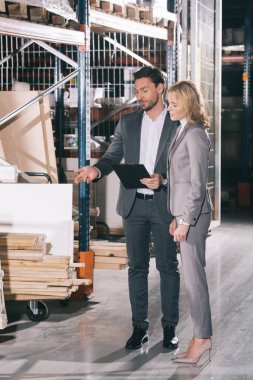 handsome businessman pointing with finger at construction materials while standing near businesswoman clipart