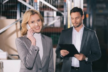 İş adamının yanında akıllı telefondan konuşurken kameraya bakan neşeli iş kadınının seçici odağı