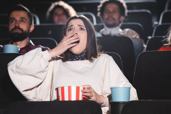 selective focus of shocked woman holding popcorn and watching movie in cinema 