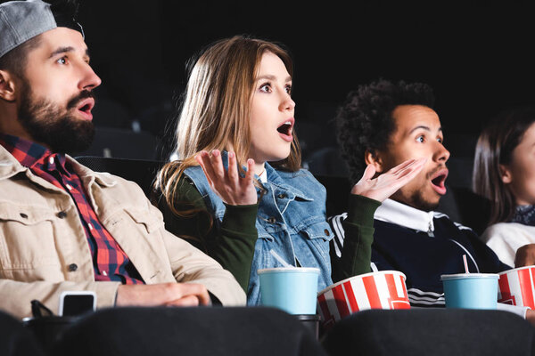 шокированные мультикультурные друзья с попкорном смотреть фильм в кино
 