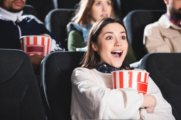 selective focus of smiling woman with popcorn watching movie in cinema 