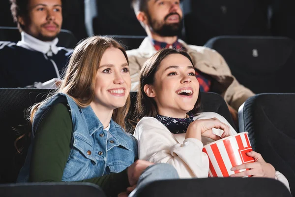selective focus of smiling friends with popcorn watching movie in cinema